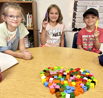 Three happy elementary students making a heart shape with cubes